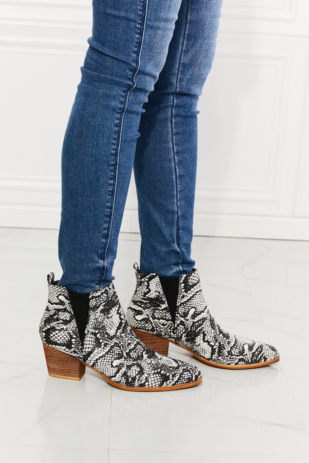 A close up of a woman in jeans wearing a pair of mid-heel pointed toe snakeskin booties 