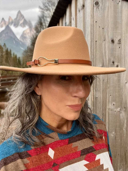 A woman wearing a tan wide brim western fedora with a leather and brass buckle hat band