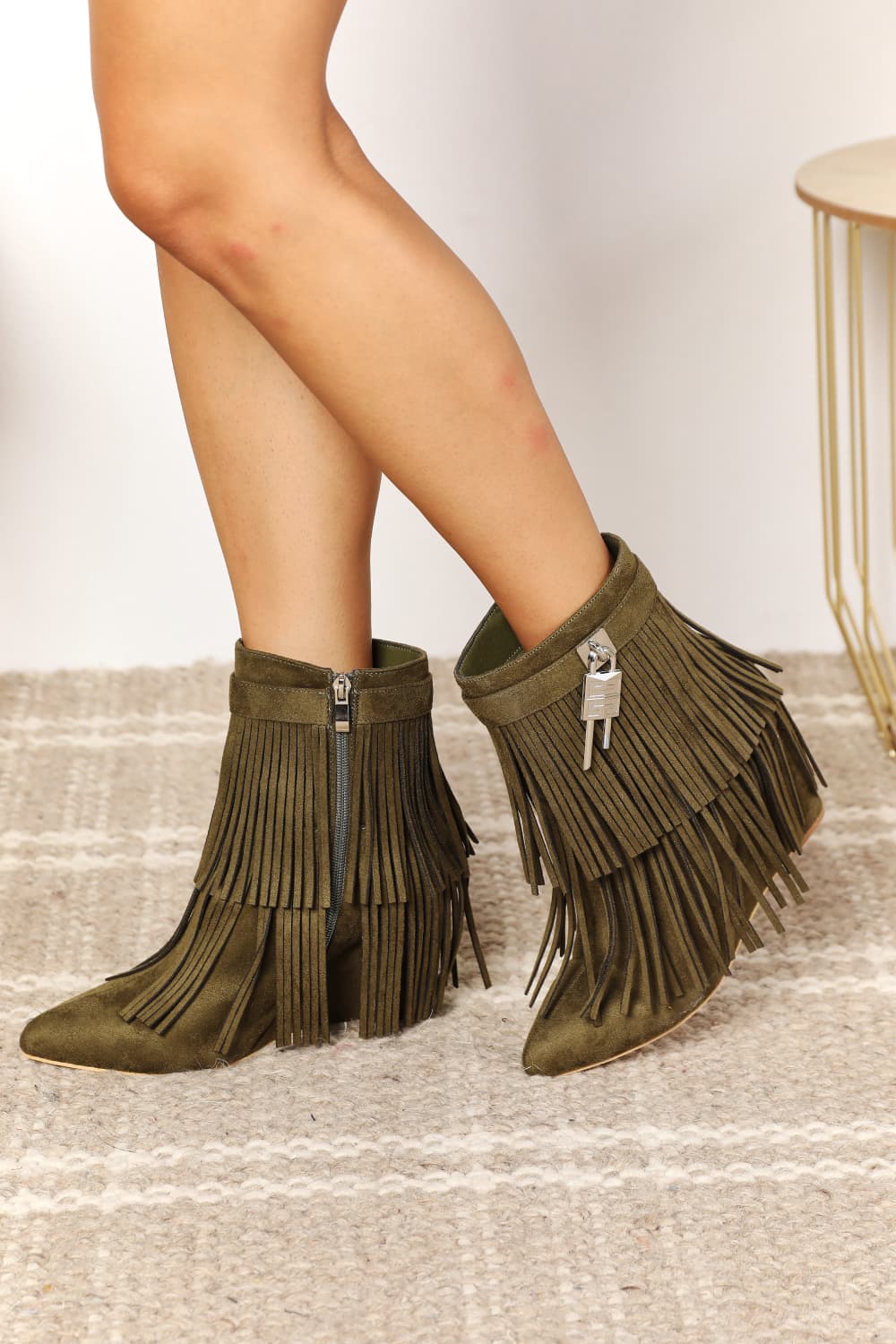 A close up of a pair of olive vegan suede wedge heel fringed ankle booties.