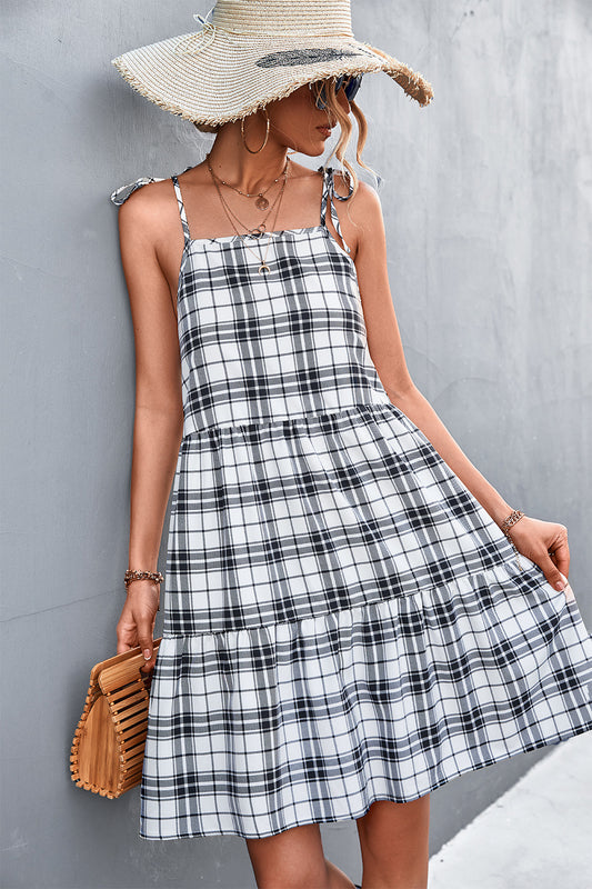 A woman wearing a black and white plaid tiered sundress with tie shoulder straps.