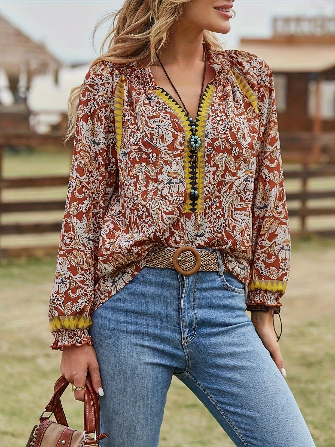 A woman wearing a brown boho style paisley print blouse with yellow contrast trim.