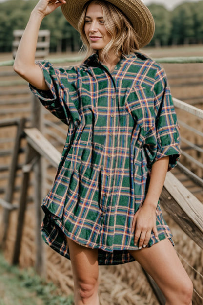 A woman wearing a hunter green plaid oversized button down shirt dress with a Western style hat and boots.