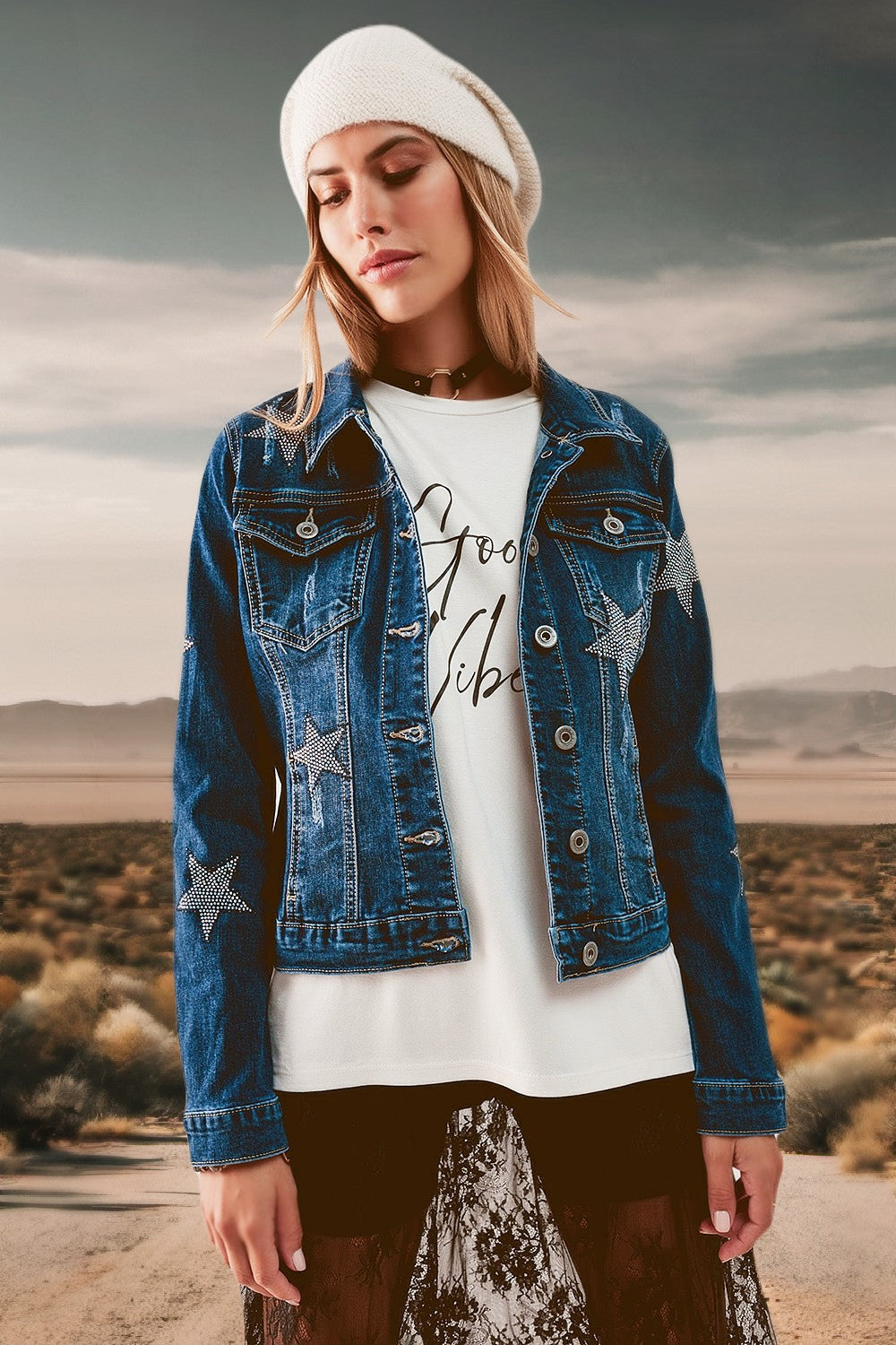 A woman standing on a desert road wearing a medium wash denim jacket embellished with stars.