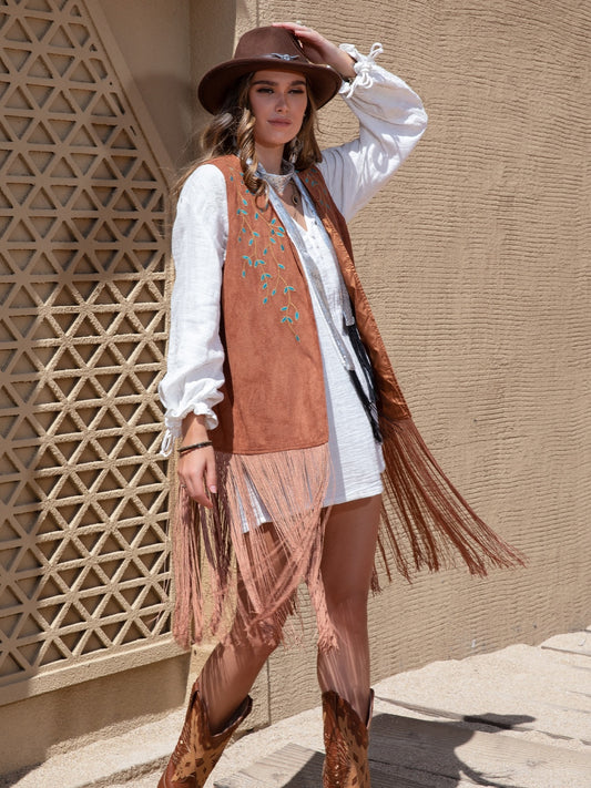 A woman wearing an open fringed vest with knee-length fringe and an embroidered design.