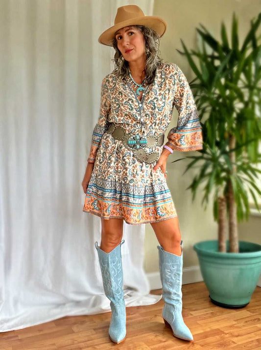 A woman wearing the Nuala boho mini dress paired with tall boots and a Western style belt and hat.