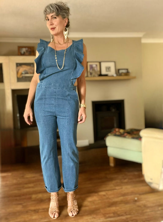 A woman standing in a room wearing a flounced sleeve denim jumpsuit