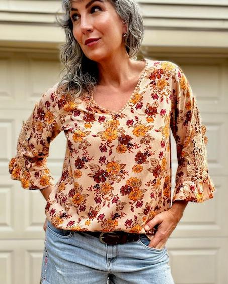 A woman wearing a flare sleeve boho blouse paired with denim shorts.