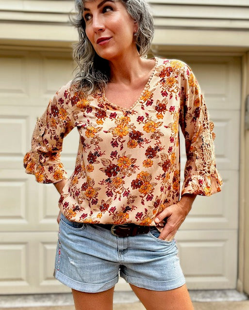 A woman wearing a flare sleeve boho blouse paired with denim shorts.