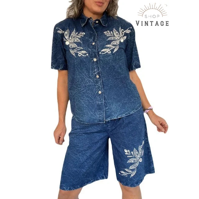 A woman wearing a 1980s era acid wash denim matching shirt and bermuda shorts set embellished with embroidery, pearls and rhinestones
