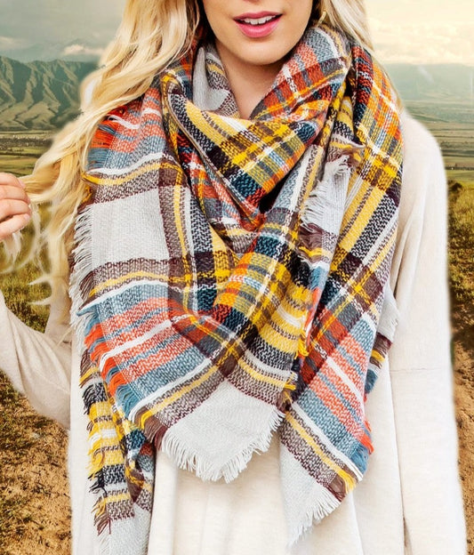 A close up of a woman standing on a country road wearing a plaid blanket scarf.