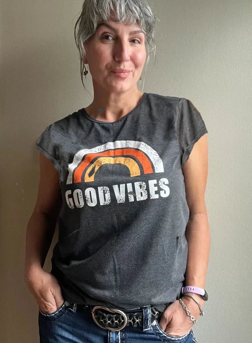 A woman wearing a retro graphic tee featuring a rainbow with the phrase "good vibes" underneath.