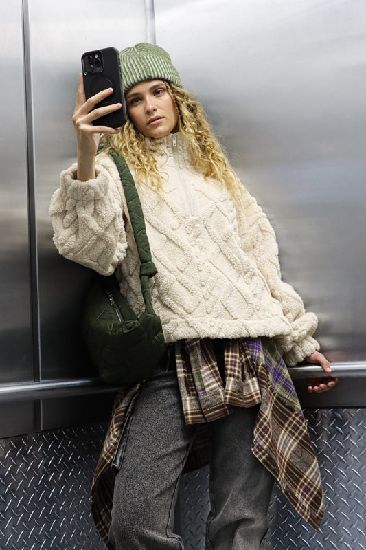 A woman taking a selfie in an elevator while wearing the Tova cable knit fuzzy fleece with a mock neck and a half zip.