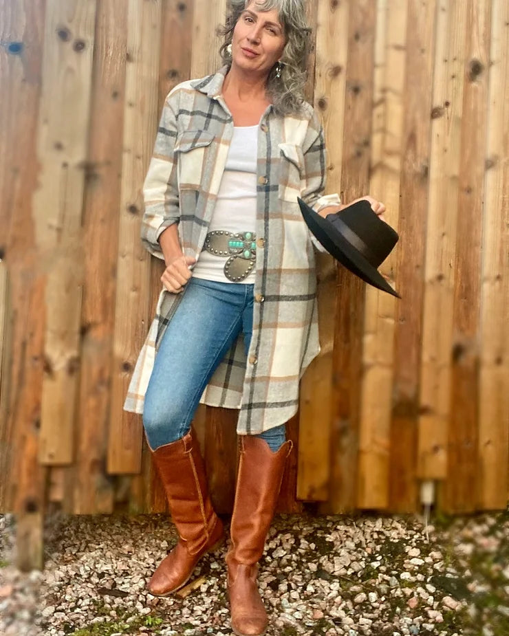 A woman wearing the Renegade Oversized Plaid Flanel shacket in grey, paired with tall leather boots.