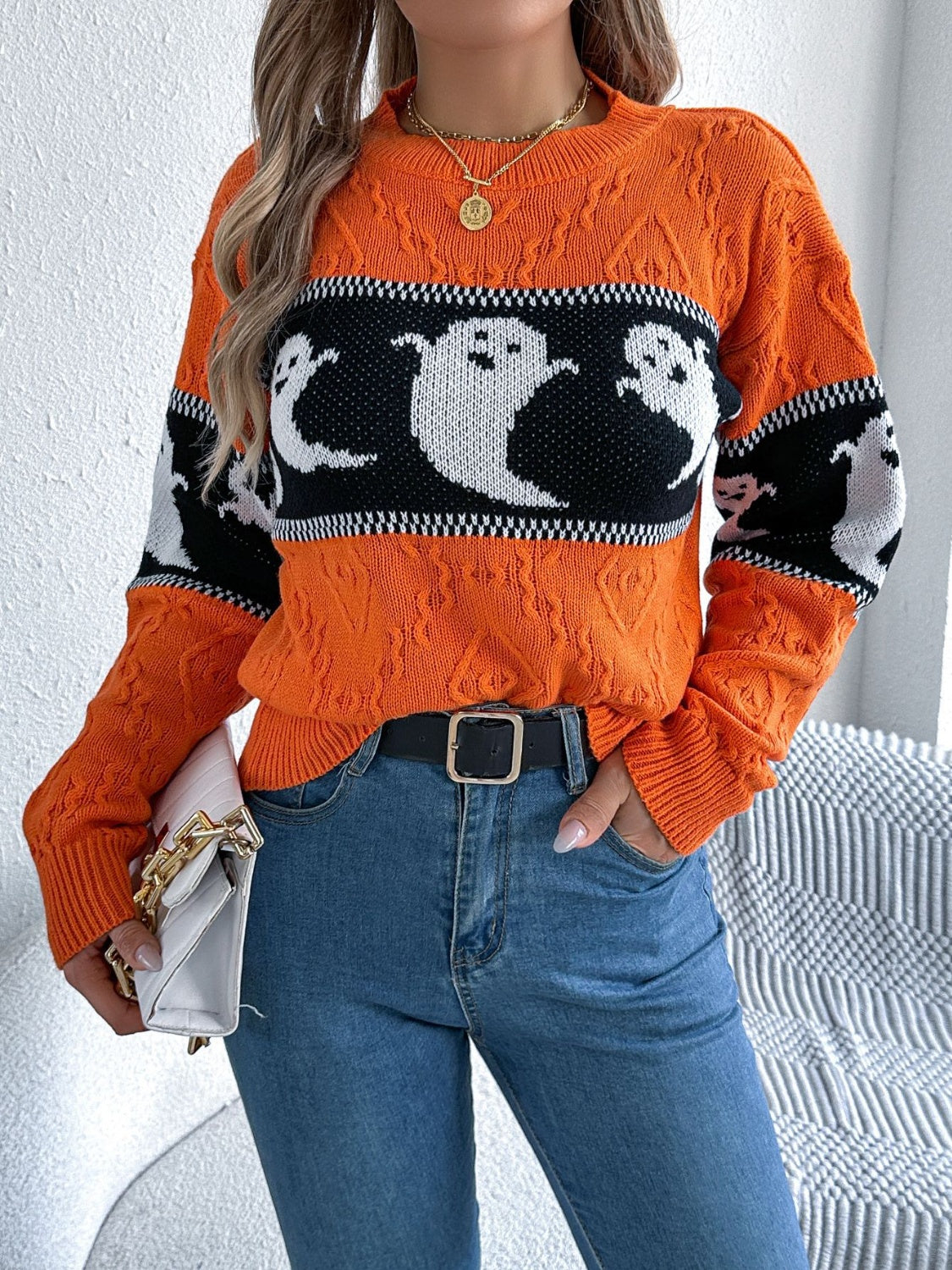 A woman wearing a textured orange pullover Halloween sweater with a black and white ghost motif across the front.