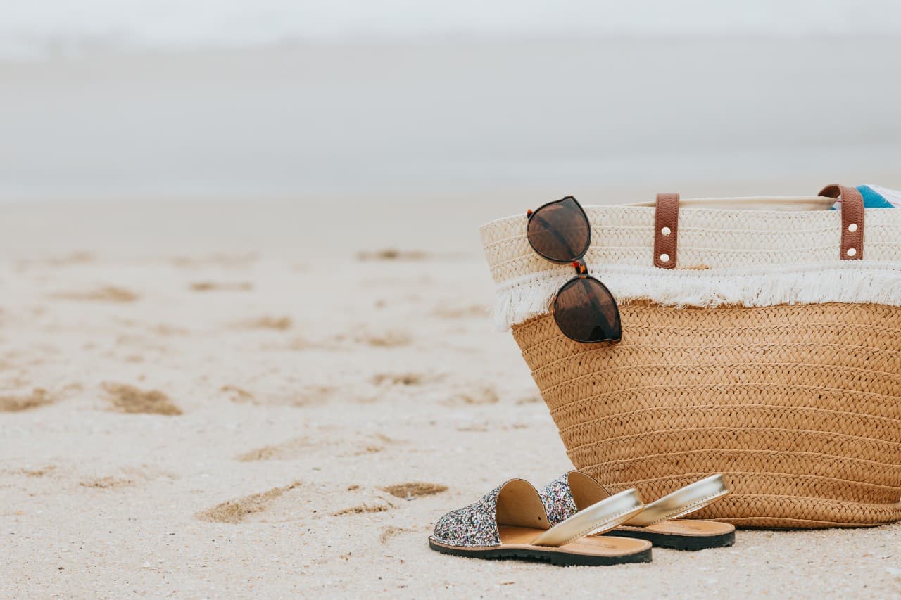 The landing page photo for the Vacation Staton, a close shot of a straw beach bag sitting on a sandy beach